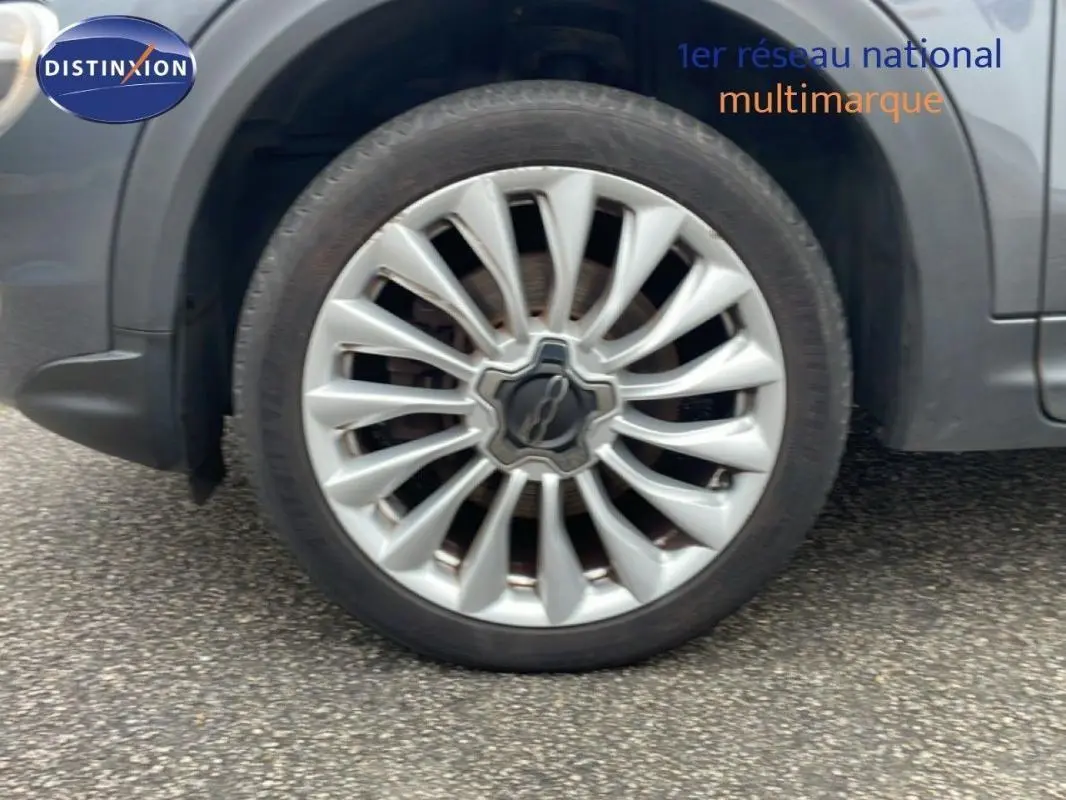 Gros plan sur la jante alliage 18 pouces argentée du côté avant droit d'une FIAT 500X gris foncé.