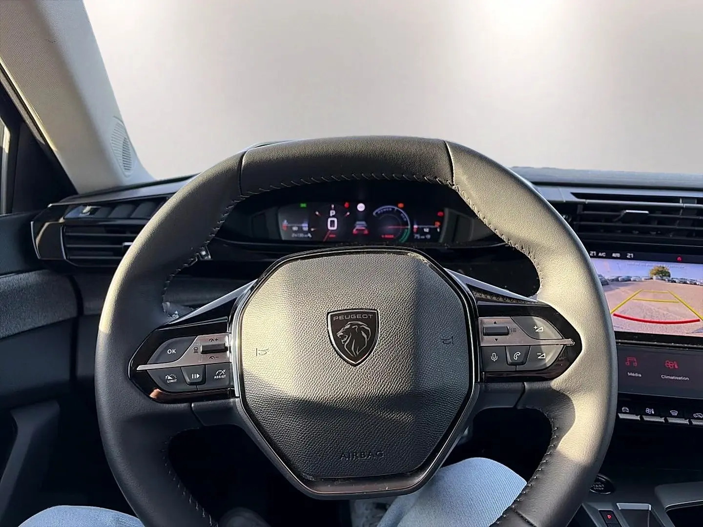 Vue intérieure centrée sur le volant cuir noir de la Peugeot 408 Hybrid 145 avec tableau de bord numérique et écran caméra de recul.