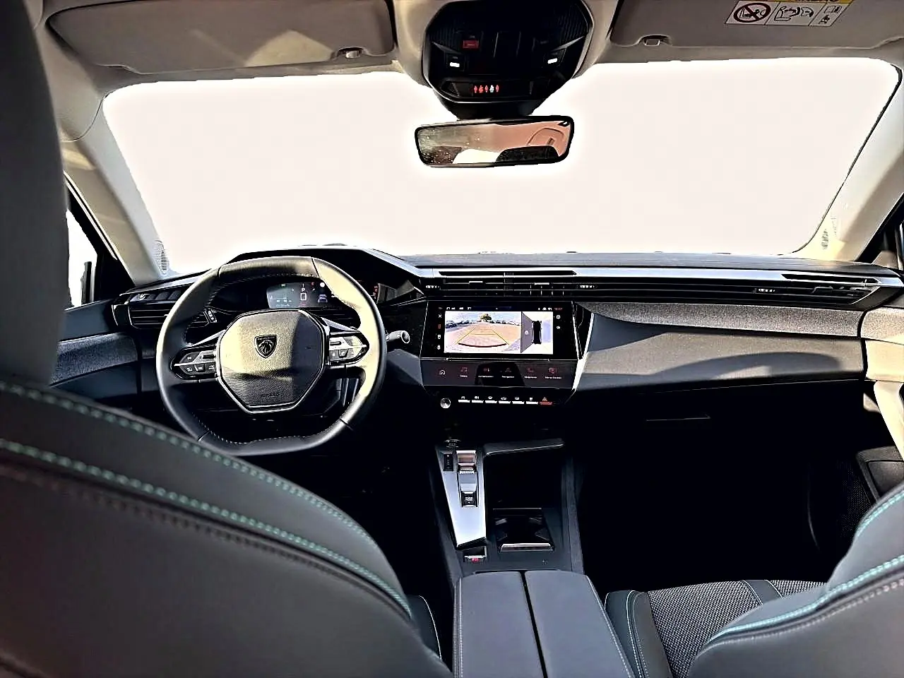 Vue intérieure avant du Peugeot 408 Hybrid noir 2025, avec tableau de bord moderne et écran tactile affichant la caméra de recul.