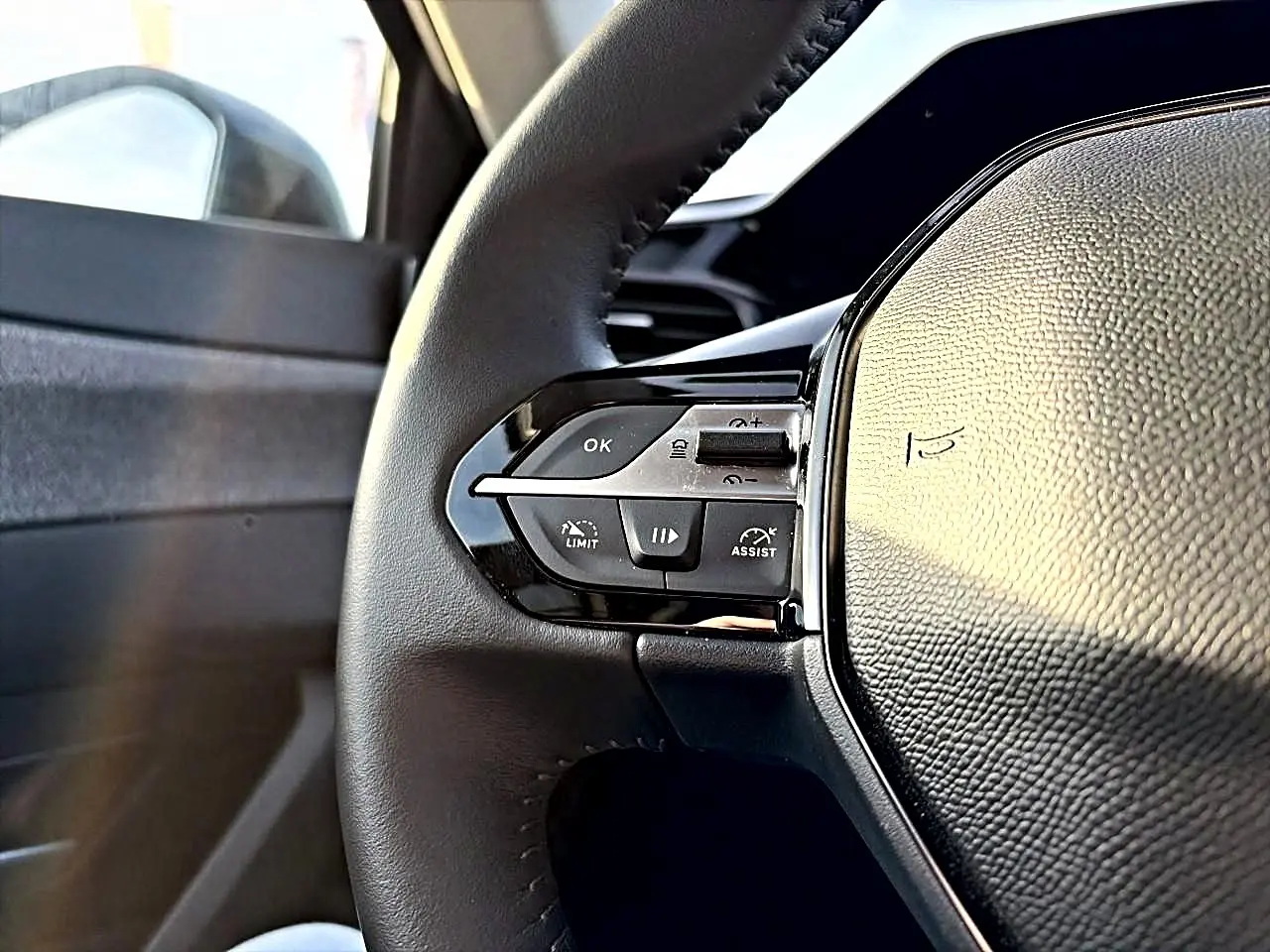 Gros plan sur le volant cuir côté gauche du Peugeot 408 Hybrid 145 allure e-dcs6 noir, avec commandes intégrées.