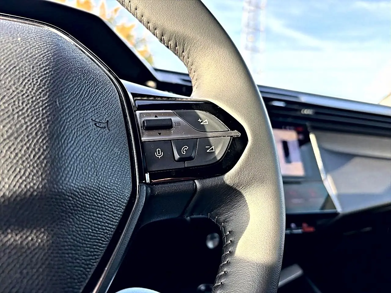 Gros plan sur le volant cuir noir de la Peugeot 408 Hybrid 145 allure e-dcs6 avec commandes vocales et multimédia visibles.