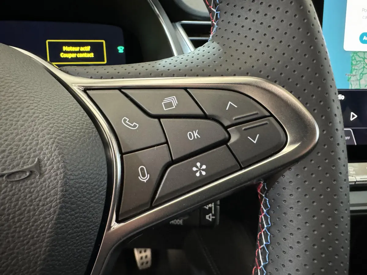 Gros plan sur les commandes multifonctions à droite du volant perforé avec surpiqûres tricolores dans un Renault Captur blanc esprit Alpine E-Tech 2025.