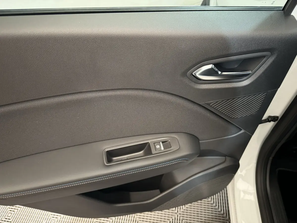 Gros plan sur la porte intérieure côté droit du Renault Captur blanc, avec couture bleue et bouton de verrouillage.