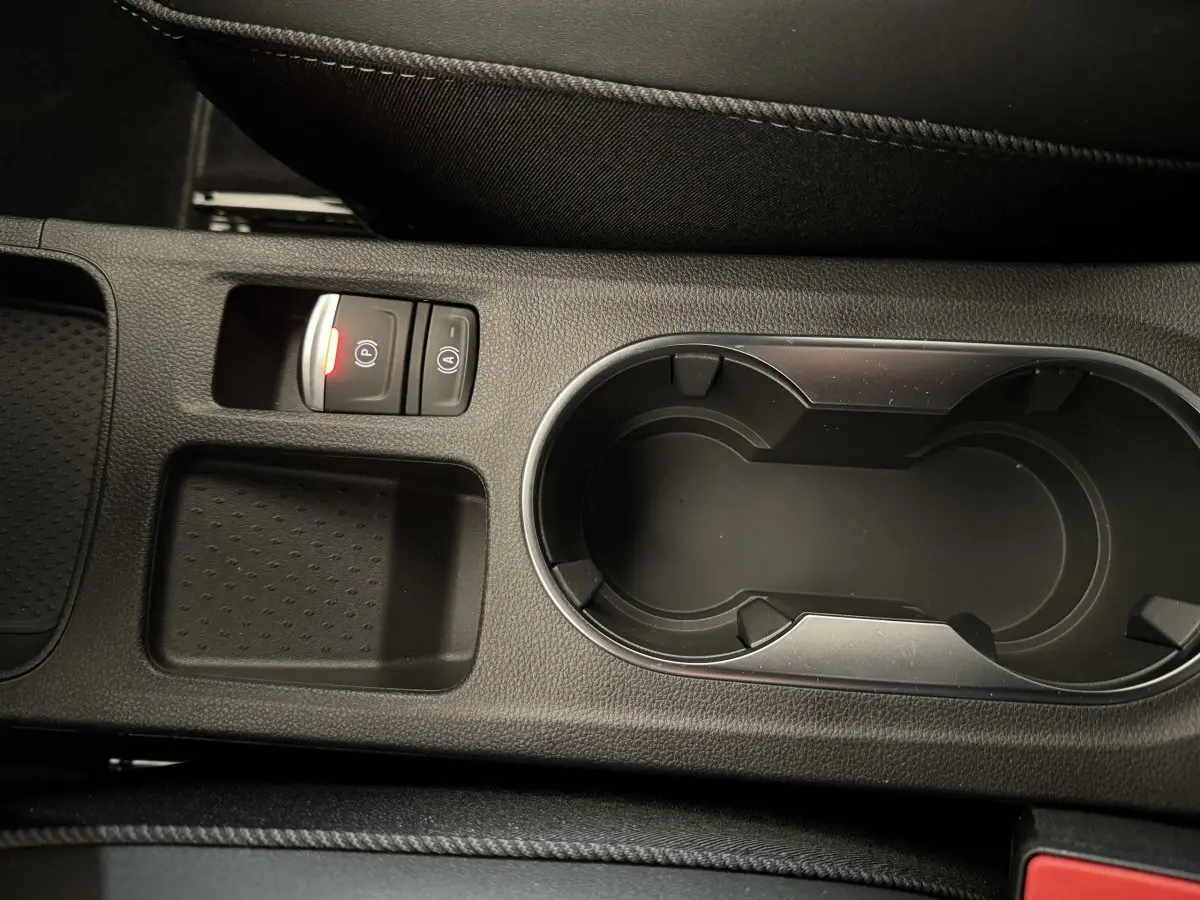 Gros plan sur la console centrale noire du Renault Captur blanc, avec porte-gobelets et bouton de frein à main électrique allumé.