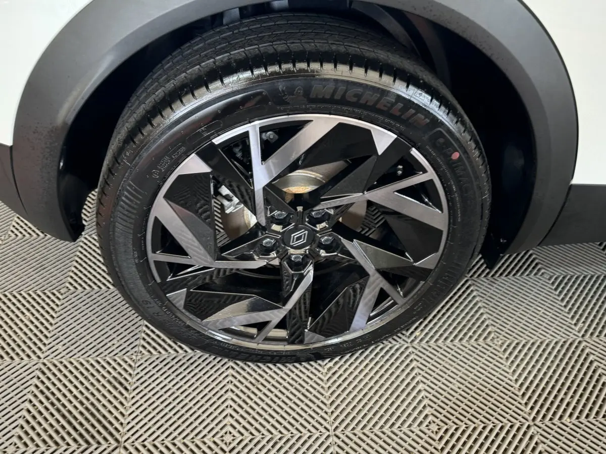 Gros plan sur la roue avant droite du Renault Captur blanc, jante alliage noire et argent au design géométrique.