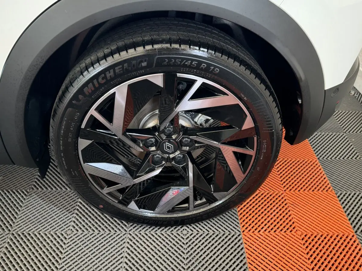 Gros plan sur la roue avant droite du Renault Captur blanc esprit Alpine E-Tech avec jante noire et argentée au design géométrique.