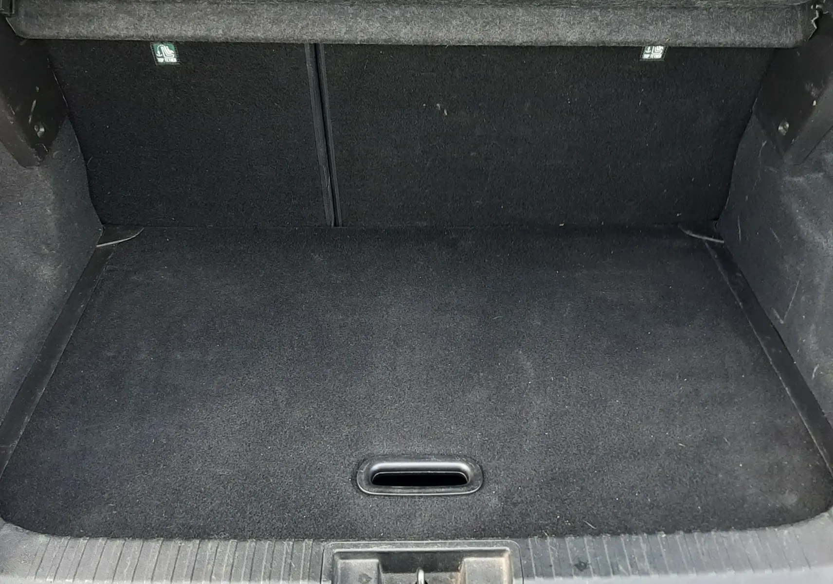 Coffre ouvert vu de l'arrière du Renault Captur blanc toit noir, espace de chargement vide et tapis noir.