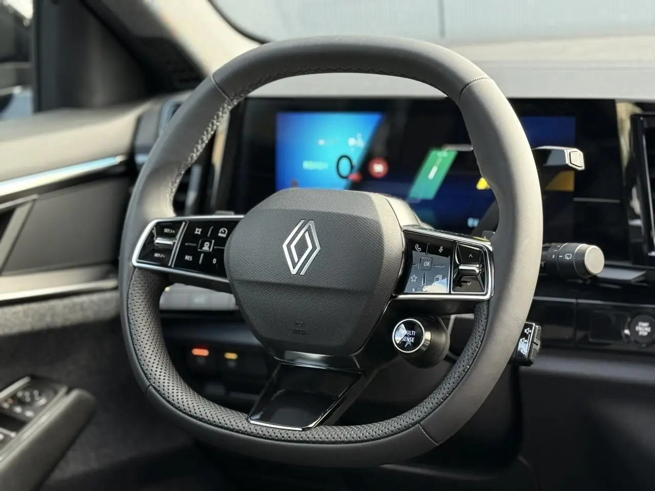Gros plan sur le volant textile noir du Renault Espace VI 6 E-Tech avec commandes intégrées et écran numérique en arrière-plan.