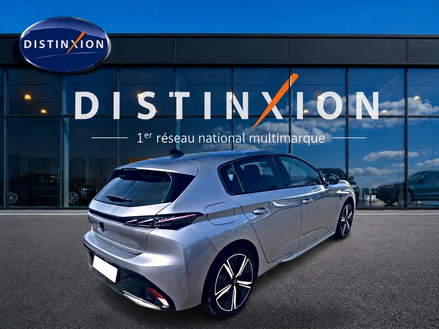 Peugeot 308 gris en vue 3/4 arrière droit, avec jantes alliage et feux arrière LED distinctifs, devant un showroom Distinxion.