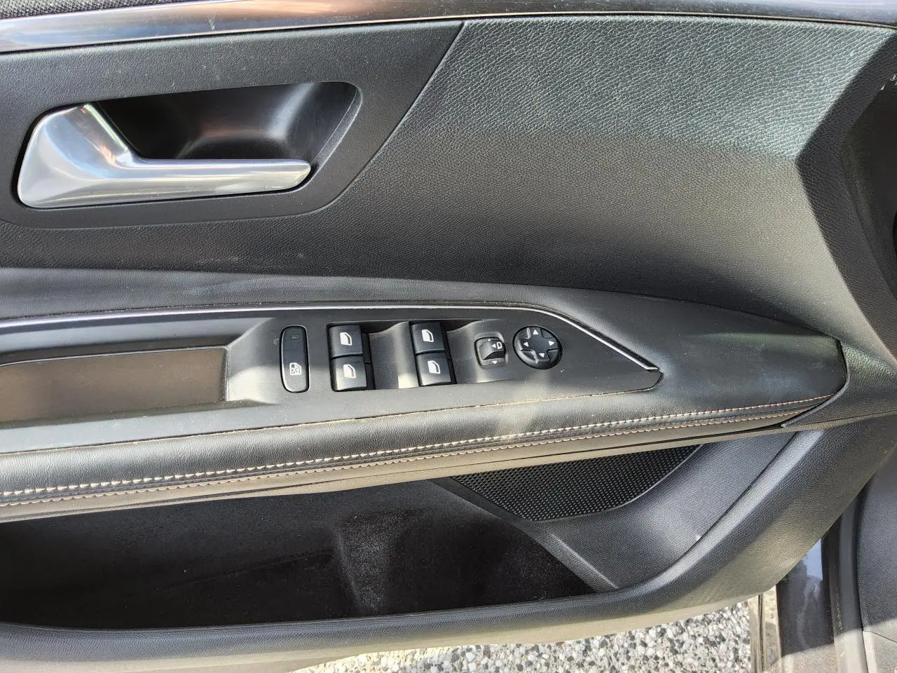 Gros plan sur la porte conducteur intérieure noire avec commandes des vitres et poignée chromée du Peugeot 3008 gris métallisé.