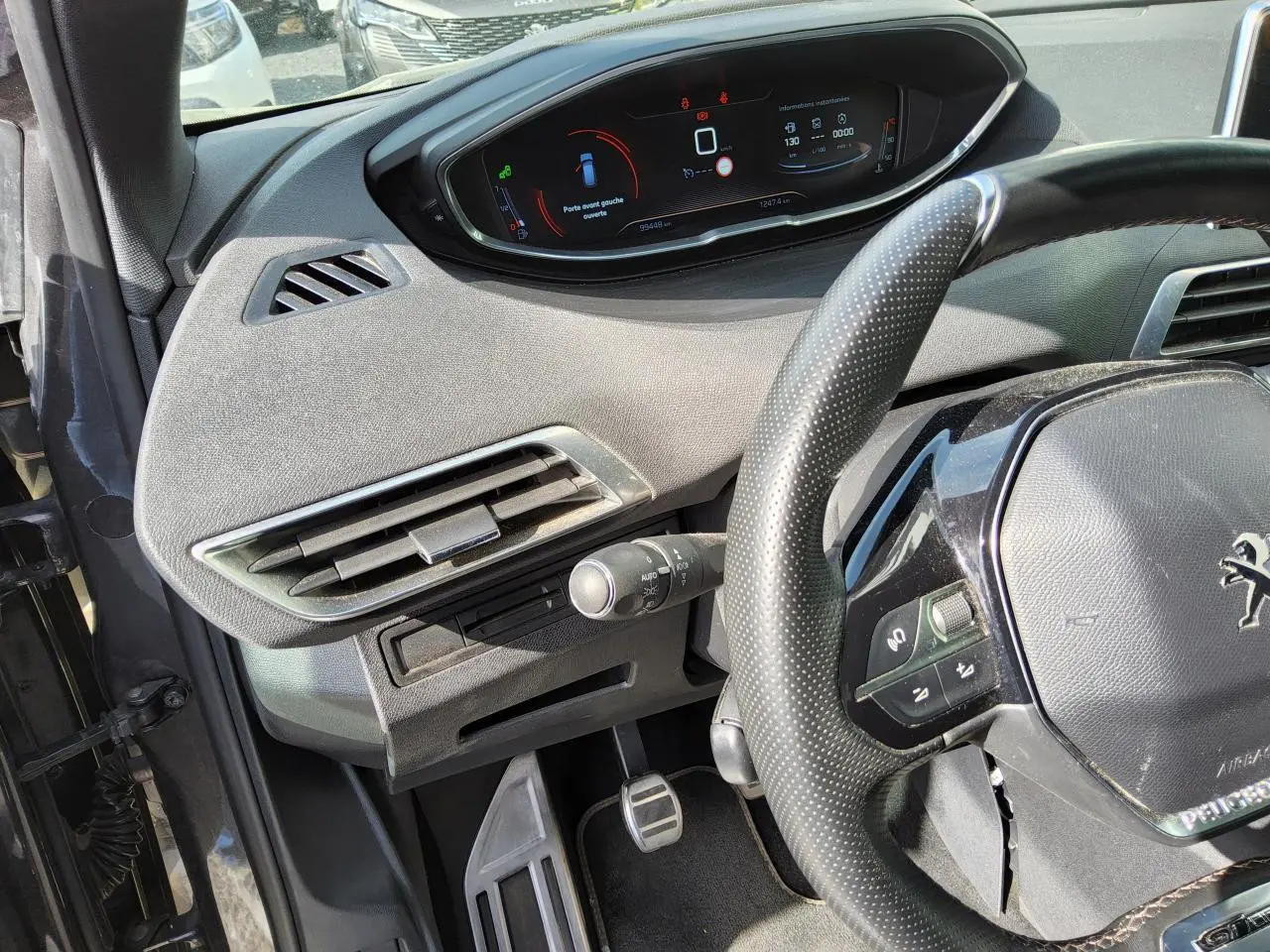 Vue rapprochée du tableau de bord et volant cuir perforé du Peugeot 3008 gris métallisé, affichage numérique et commandes au volant visibles.