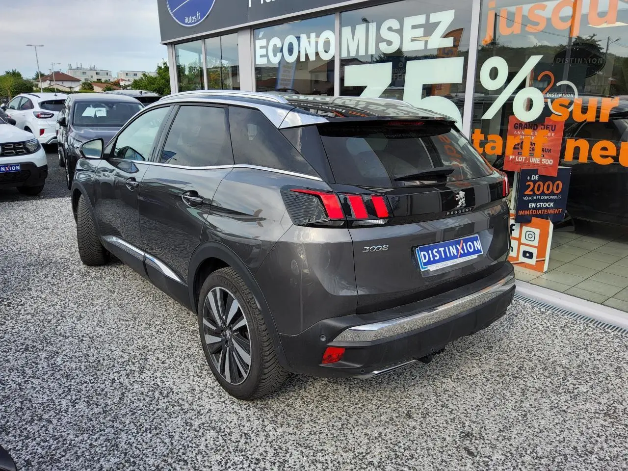 Vue 3/4 arrière droite d'un Peugeot 3008 gris métallisé avec jantes alliage et toit noir devant une vitrine commerciale.