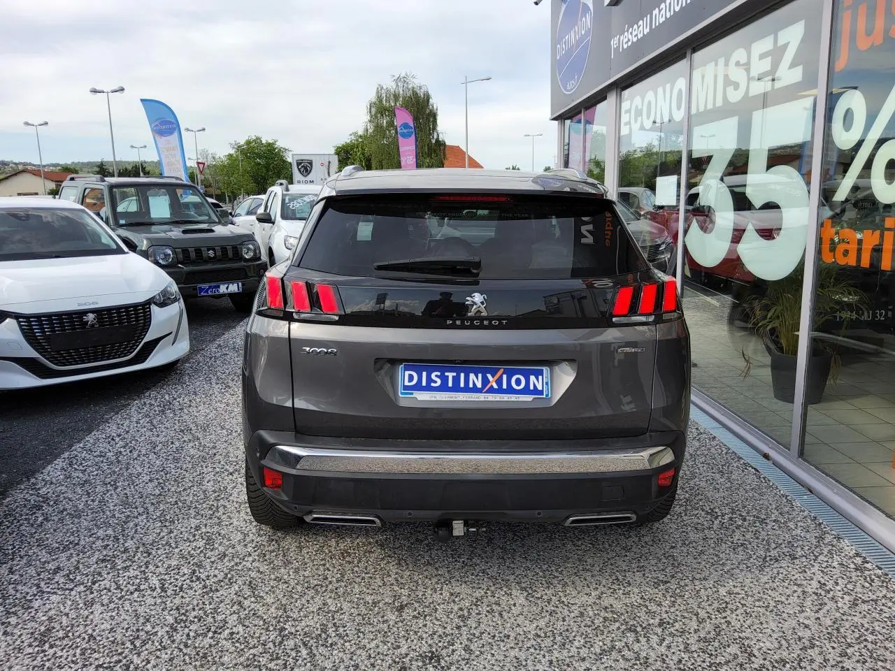 Vue arrière d'un Peugeot 3008 gris métallisé avec barres de toit et attelage visible sur parking de concession.