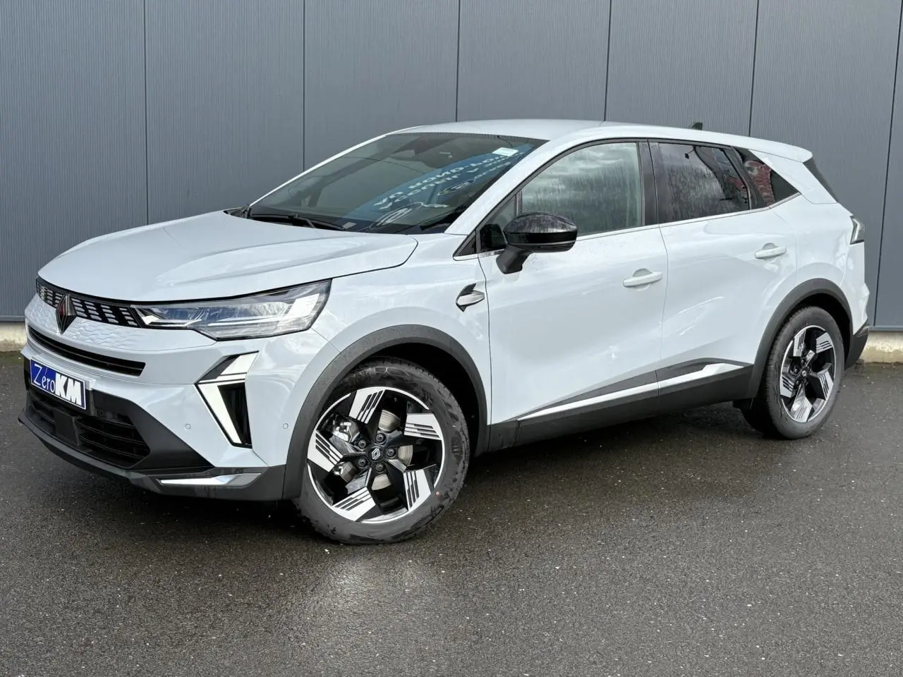 Renault Symbioz gris clair en 3/4 avant droit, avec jantes noires et blanches et calandre moderne lumineuse.