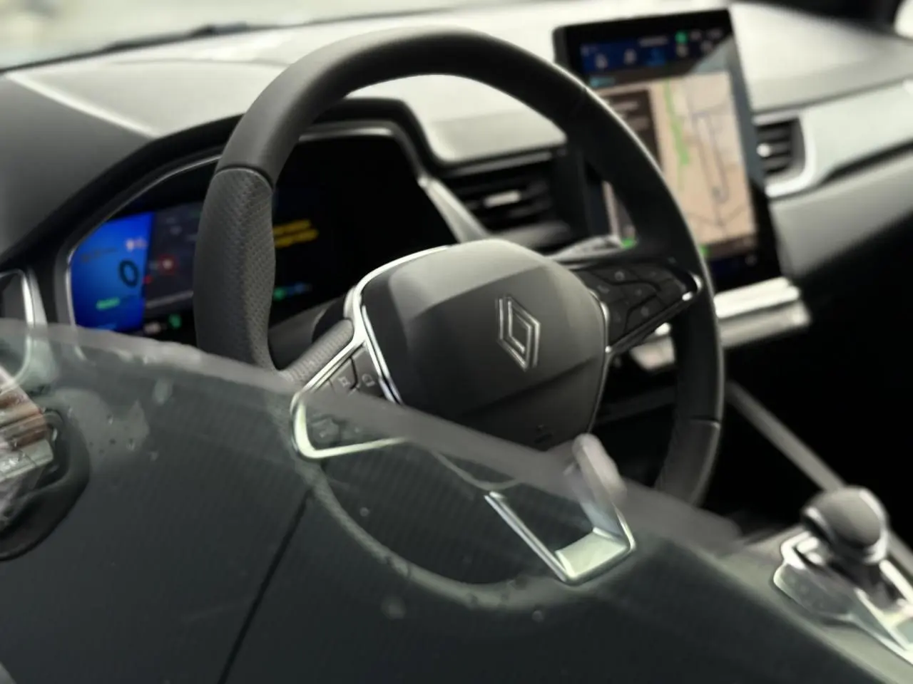 Vue intérieure rapprochée du volant en cuir et de l'écran tactile vertical du tableau de bord du Renault Symbioz gris Rafale.
