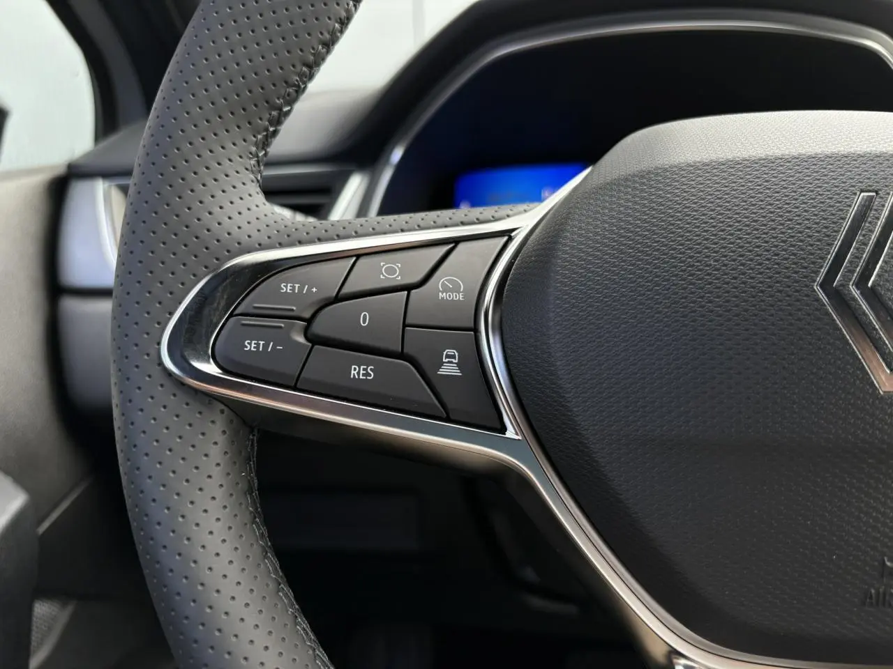 Gros plan sur le côté gauche du volant en cuir perforé gris du Renault Symbioz gris Rafale avec commandes intégrées.