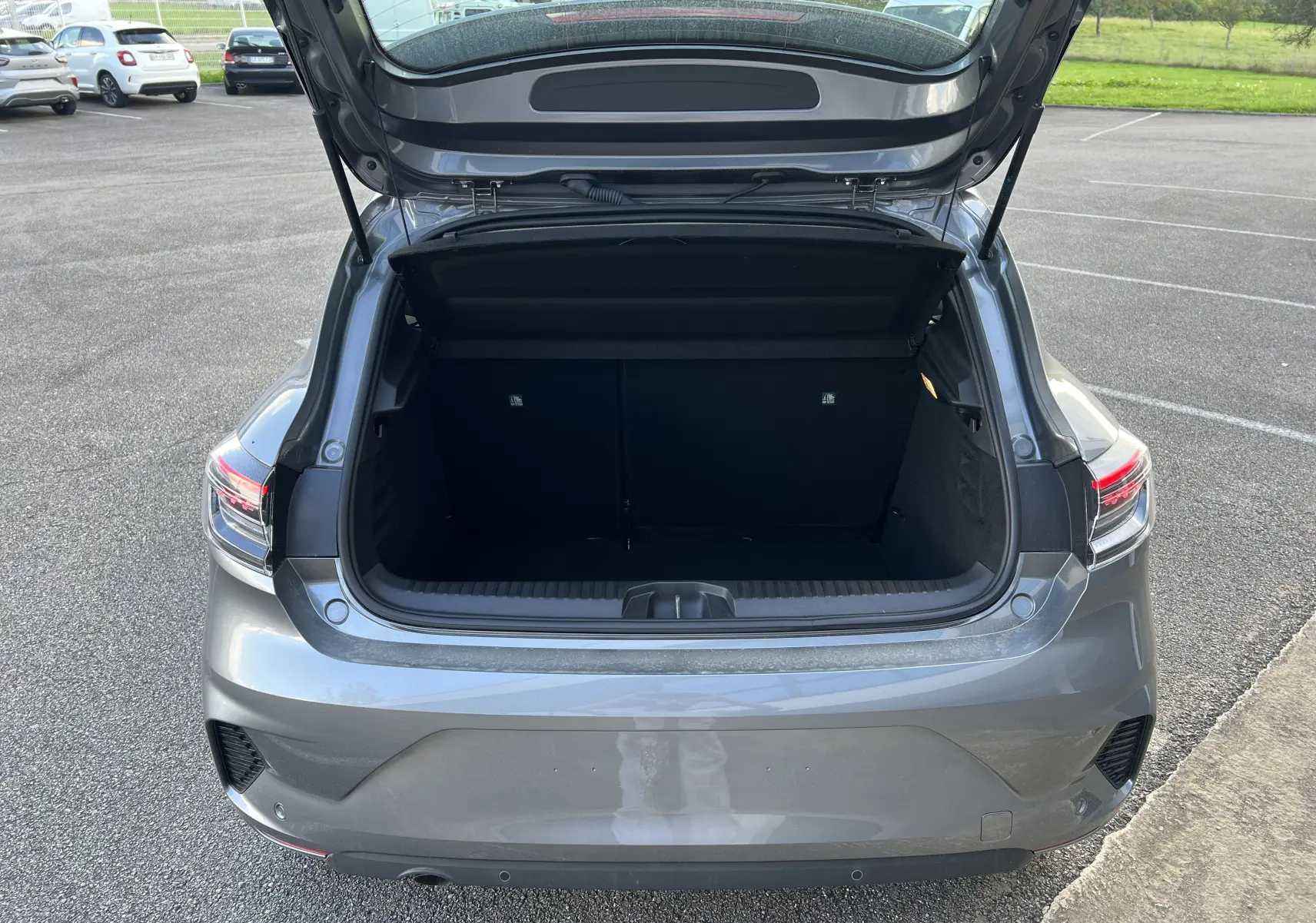 Coffre ouvert vu de l'arrière d'une Renault Clio V gris schiste avec feux arrière LED et protections chromées.