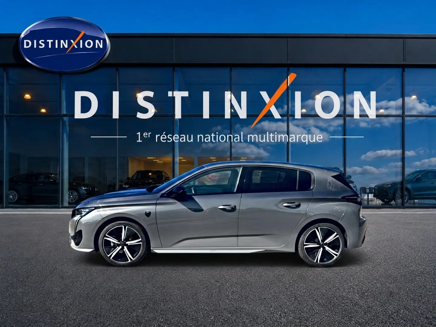 Profil droit d'une Peugeot 308 gris métallisé 2025 garée devant une vitrine avec logo Distinxion.