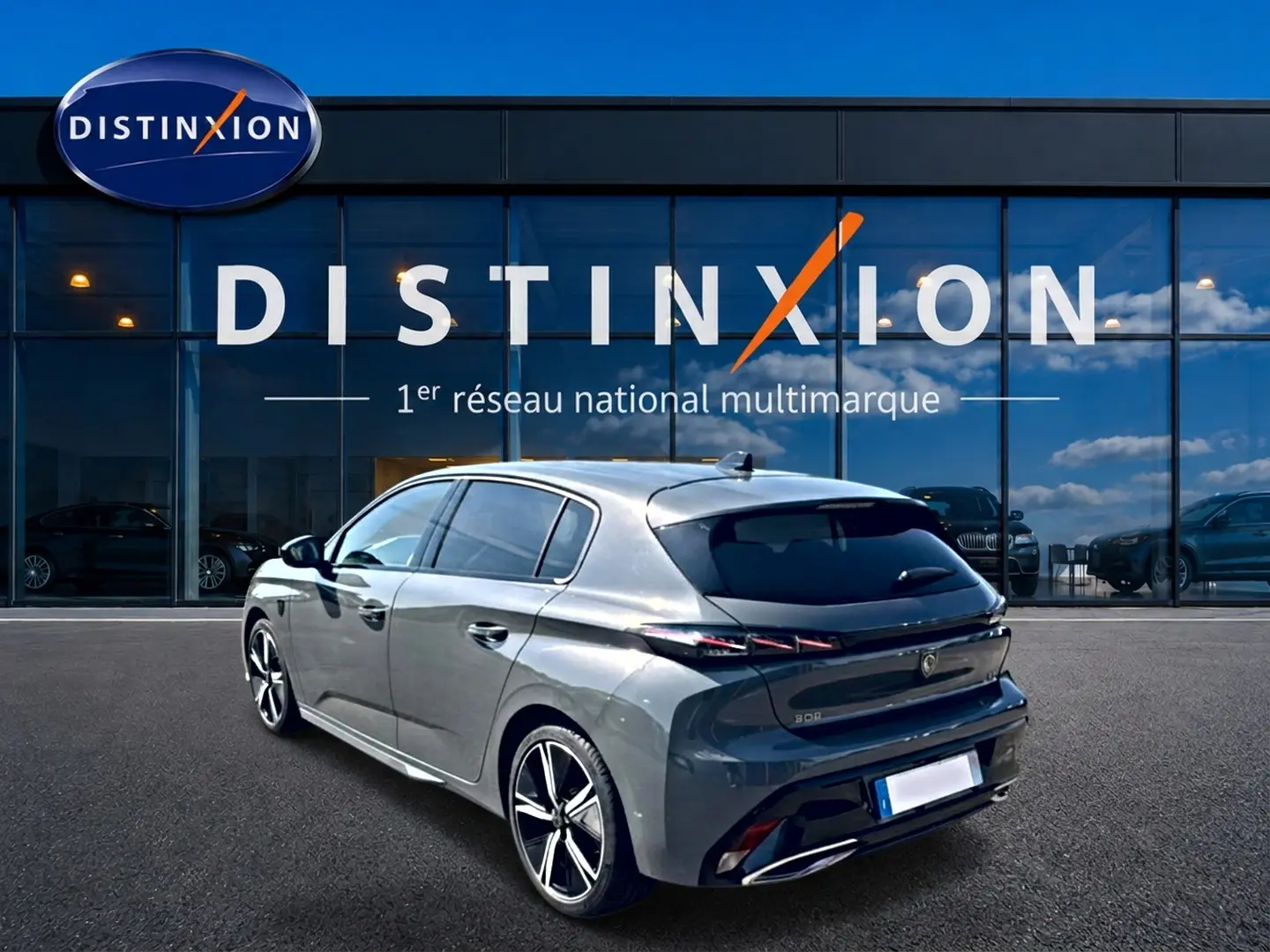 Peugeot 308 gris vue 3/4 arrière droit, jantes alu noires et vitres arrière surteintées devant showroom Distinxion.