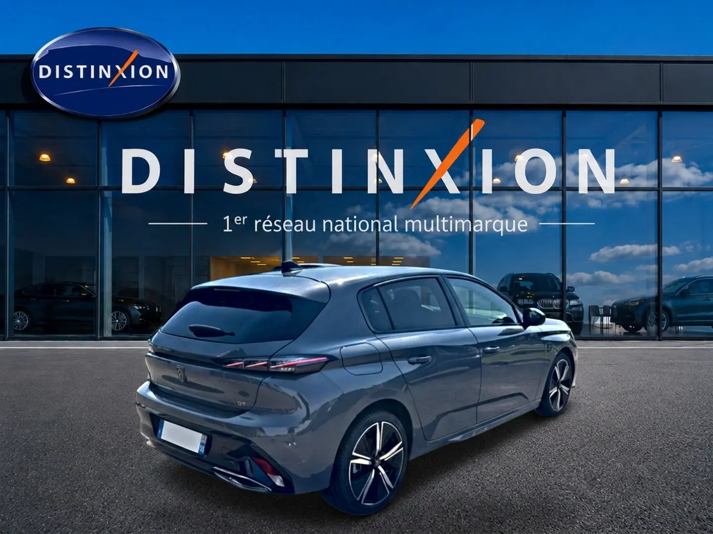 Vue 3/4 arrière droite d'une Peugeot 308 gris métallisé avec jantes alliage, stationnée devant un showroom Distinxion.