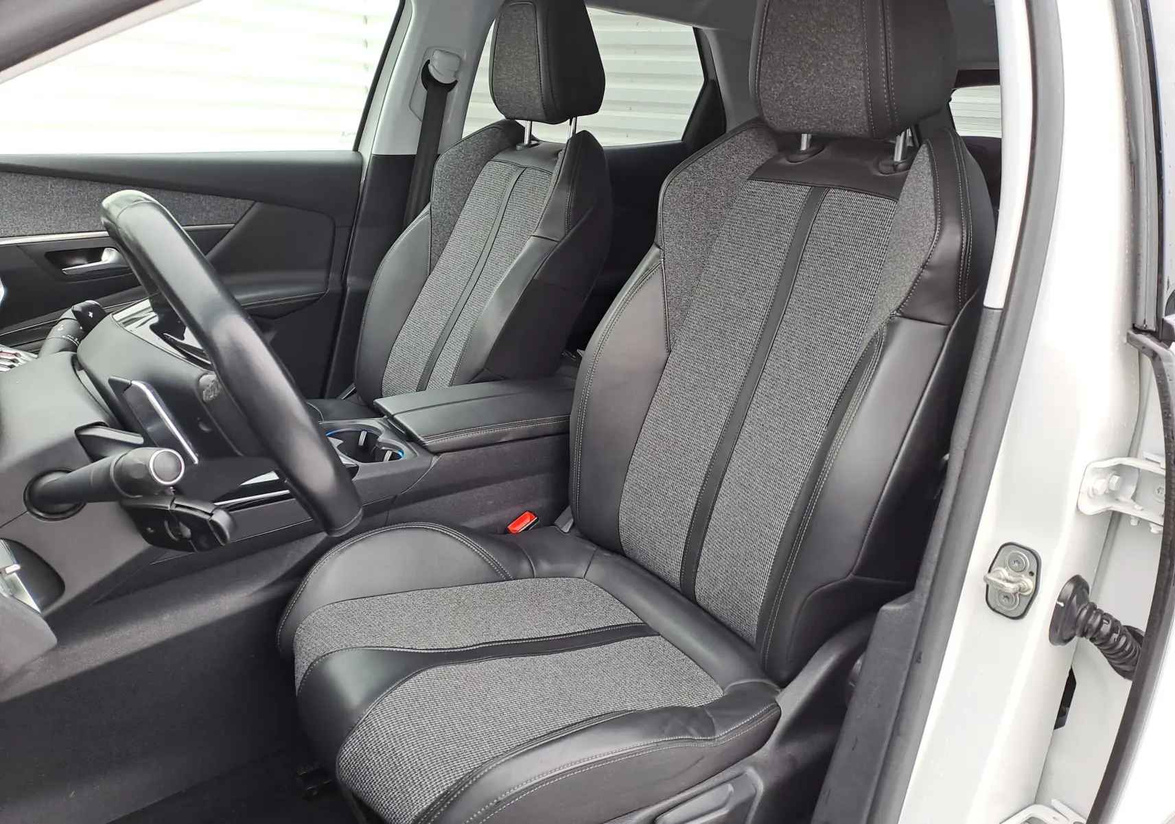 Vue intérieure côté conducteur du Peugeot 3008 blanc 2018, sièges bi-matière cuir et tissu gris avec volant noir.