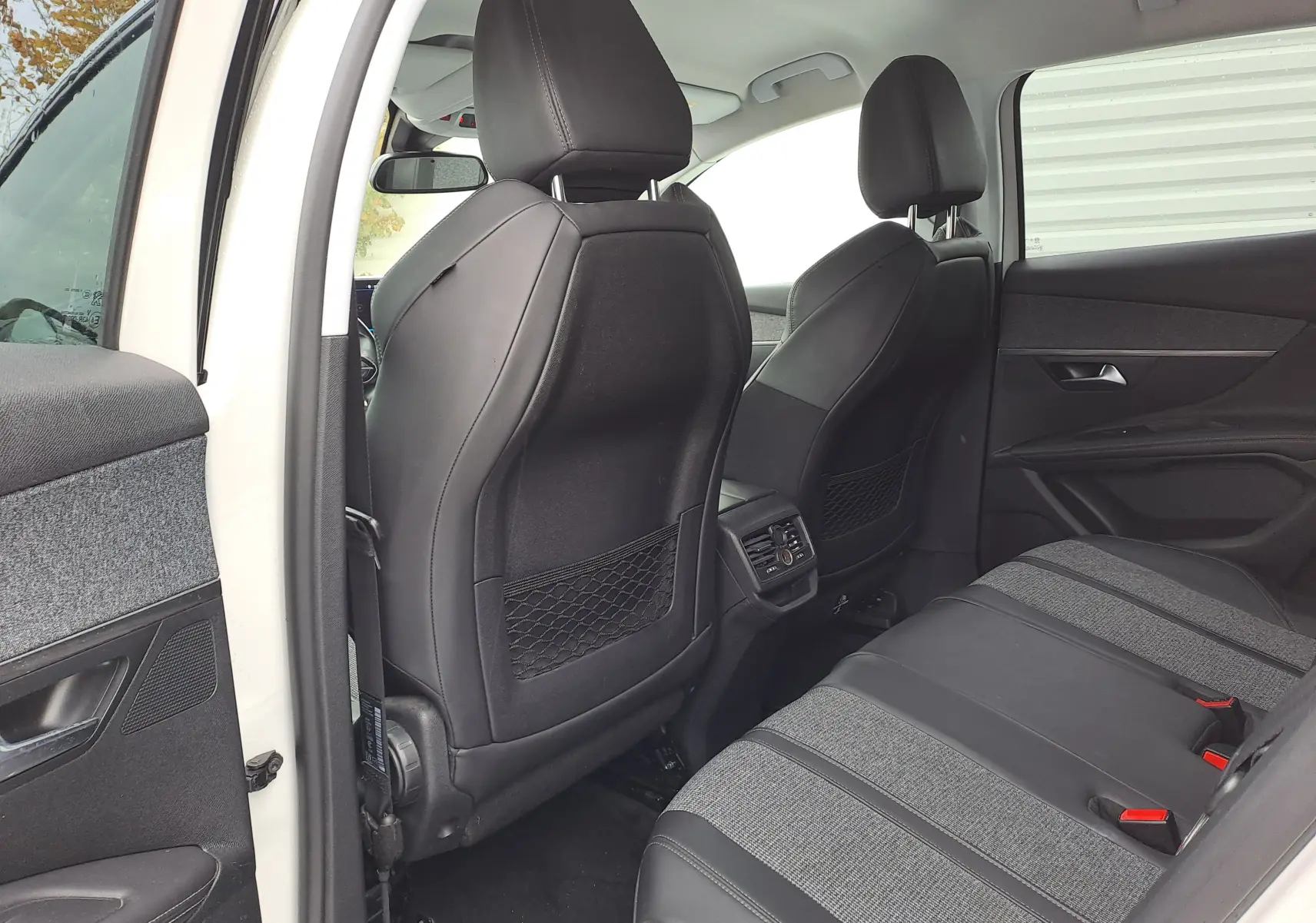 Vue intérieure arrière côté gauche d'un Peugeot 3008 blanc de 2018, sièges en tissu gris et cuir noir avec aérateurs centraux.