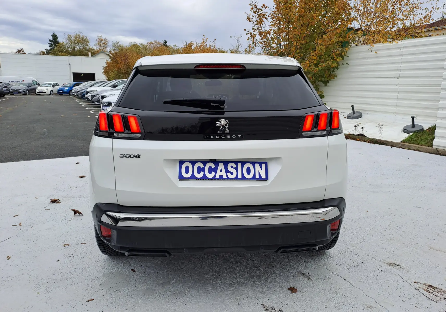 Vue arrière d'un Peugeot 3008 blanc avec feux arrière allumés et plaque "OCCASION" sur un parking extérieur.