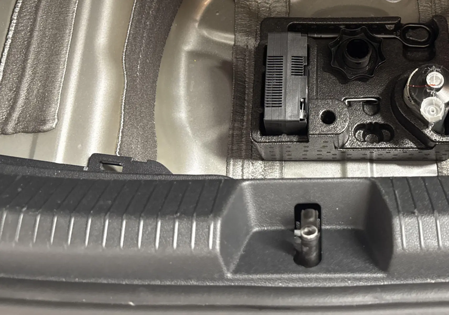 Coffre ouvert d'un Volkswagen Taigo gris cendré montrant le rangement pour outils et compresseur intégré.