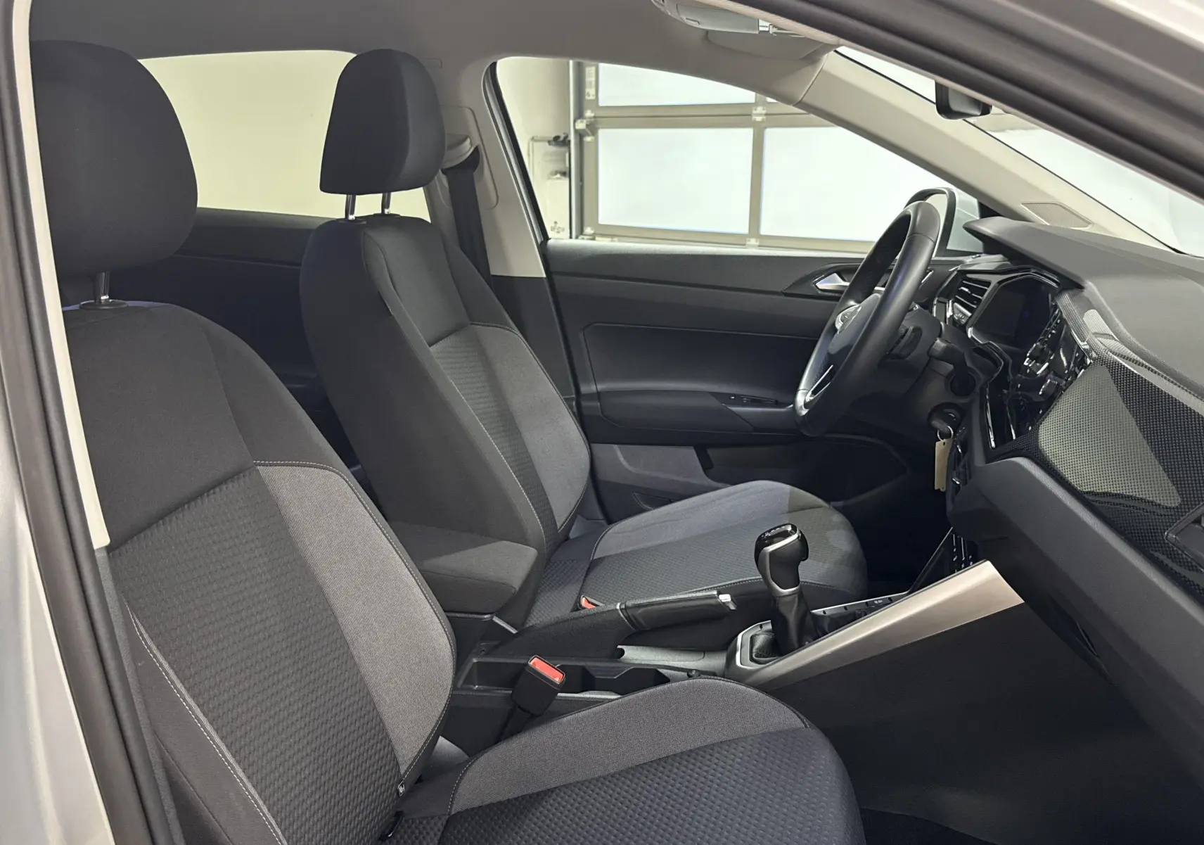 Intérieur avant du Volkswagen Taigo gris cendré 2024, sièges tissu gris et tableau de bord moderne avec volant noir.