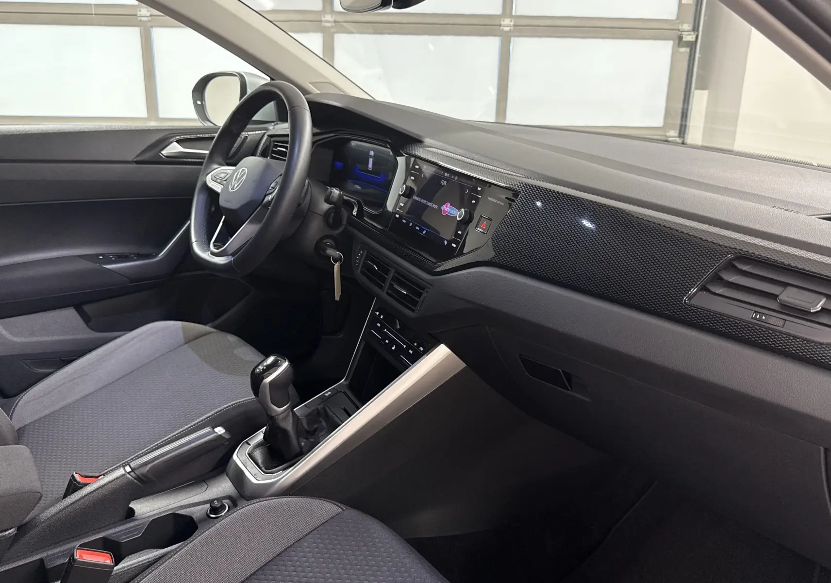 Intérieur avant droit du Volkswagen Taigo 2024, tableau de bord noir avec écran tactile et sièges tissu gris.