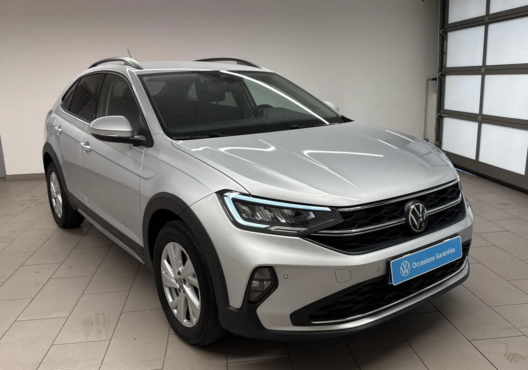 Volkswagen Taigo gris cendré en 3/4 avant droit, avec calandre noire et jantes argentées dans un garage lumineux