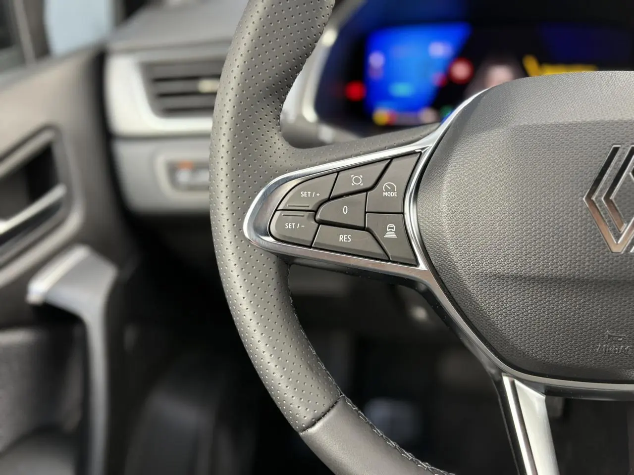 Gros plan sur le volant en cuir gris perforé de la Renault Symbioz 2025 avec commandes multifonctions et logo au centre.