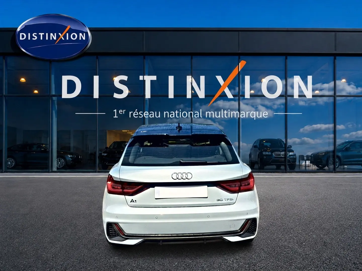 Vue arrière d'une Audi A1 Sportback 30 TFSI gris arrow avec feux LED et diffuseur noir, stationnée devant un showroom Distinxion.