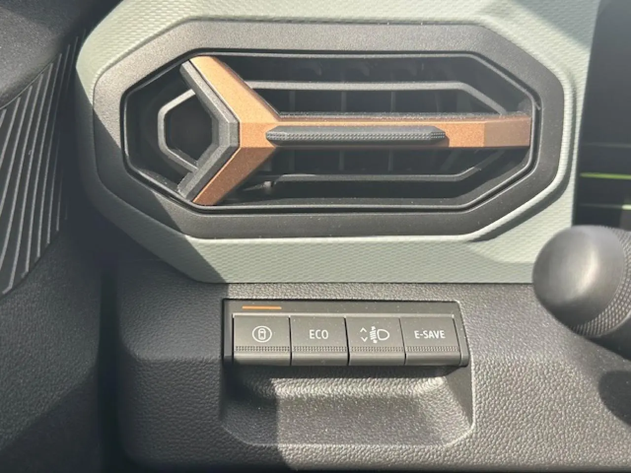 Gros plan sur la commande éco-mode et la sortie d'air hexagonale intérieure du Dacia Duster 2025 gris schiste.