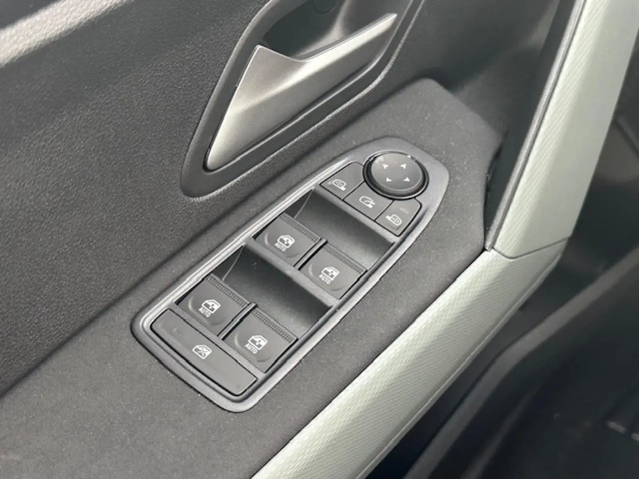 Gros plan sur les commandes des vitres électriques côté conducteur du Dacia Duster III gris schiste, intérieur moderne et épuré.