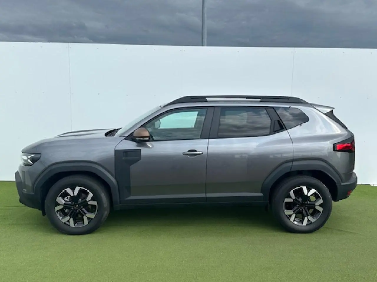 Profil côté gauche du Dacia Duster III gris schiste métallisé avec jantes alliage et barres de toit noires.