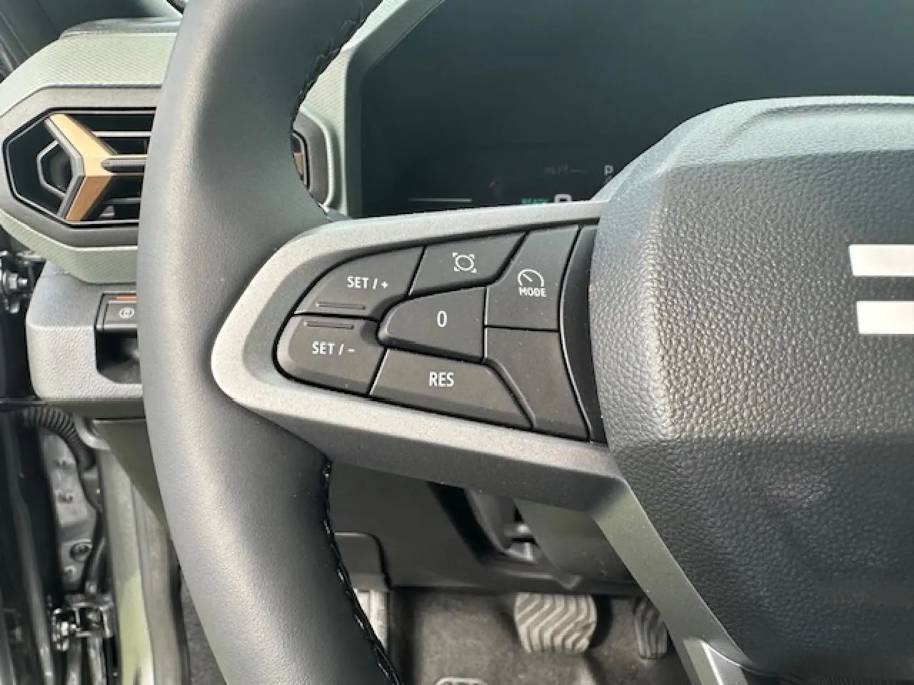 Gros plan sur les commandes au volant côté gauche du Dacia Duster III gris schiste, avec tableau de bord digital en arrière-plan.