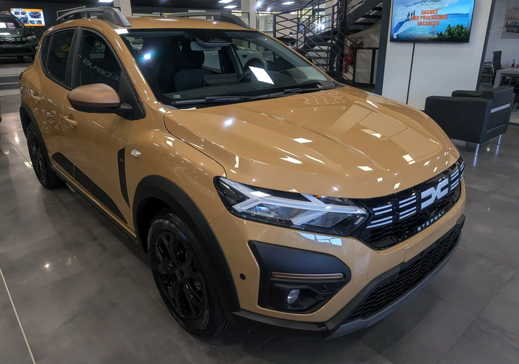 Vue 3/4 avant droite d'une Dacia Sandero Stepway beige Safari avec jantes noires et détails noirs contrastants.