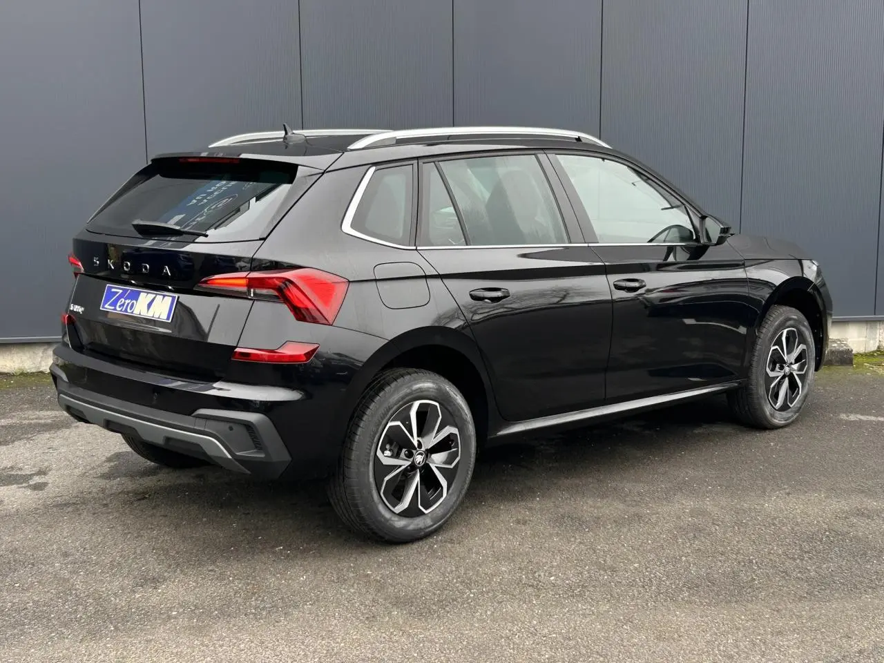 Vue 3/4 arrière droite d'un Skoda Kamiq noir Magic avec jantes alliage et baguettes chromées visibles.