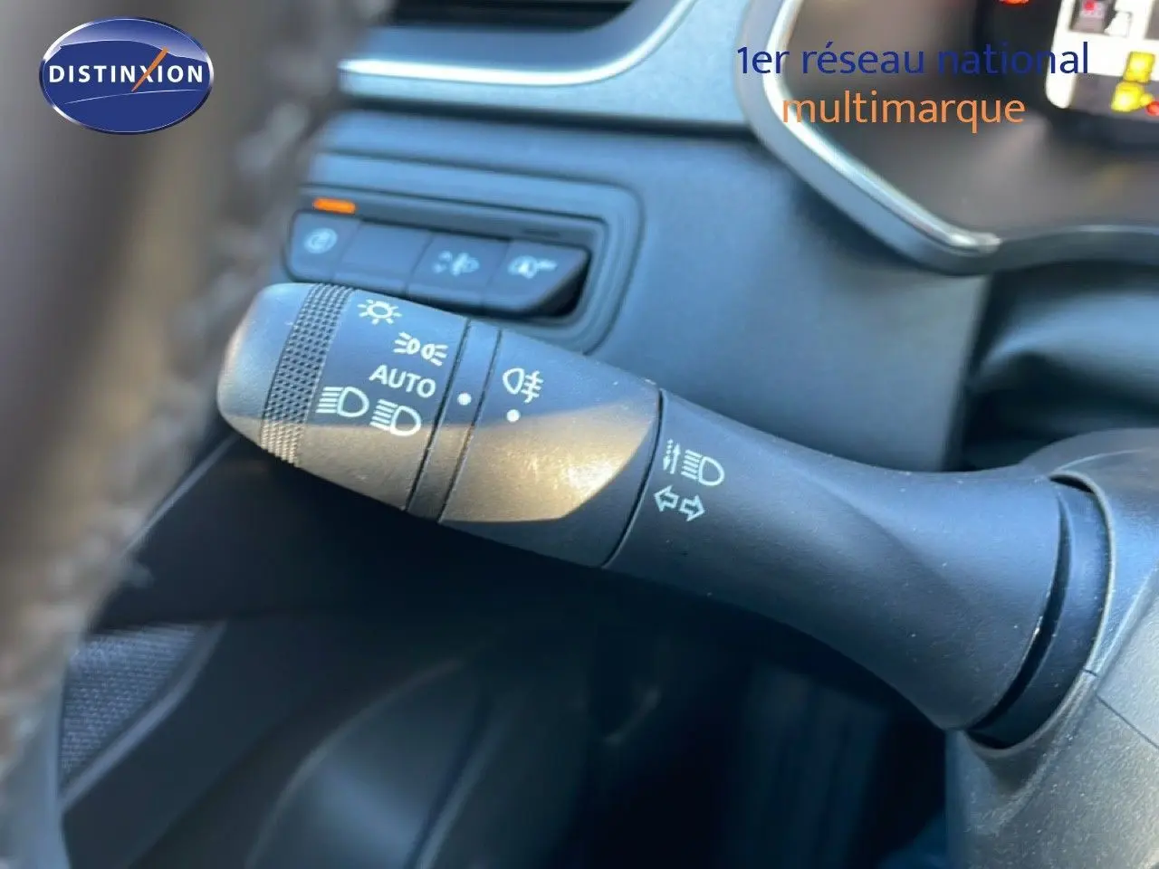 Gros plan sur la manette de commande d'éclairage à gauche du volant dans l'habitacle d'un Renault Captur rouge désir métal avec toit noir.
