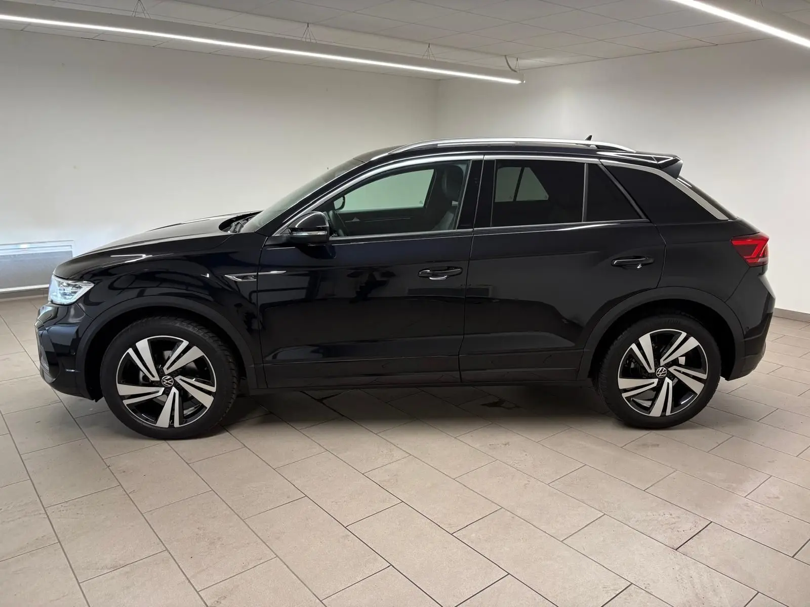 Vue de profil côté gauche du Volkswagen T-Roc 1.5 TSI 150 DSG7 R-Line Edition noir intense dans un intérieur neutre.
