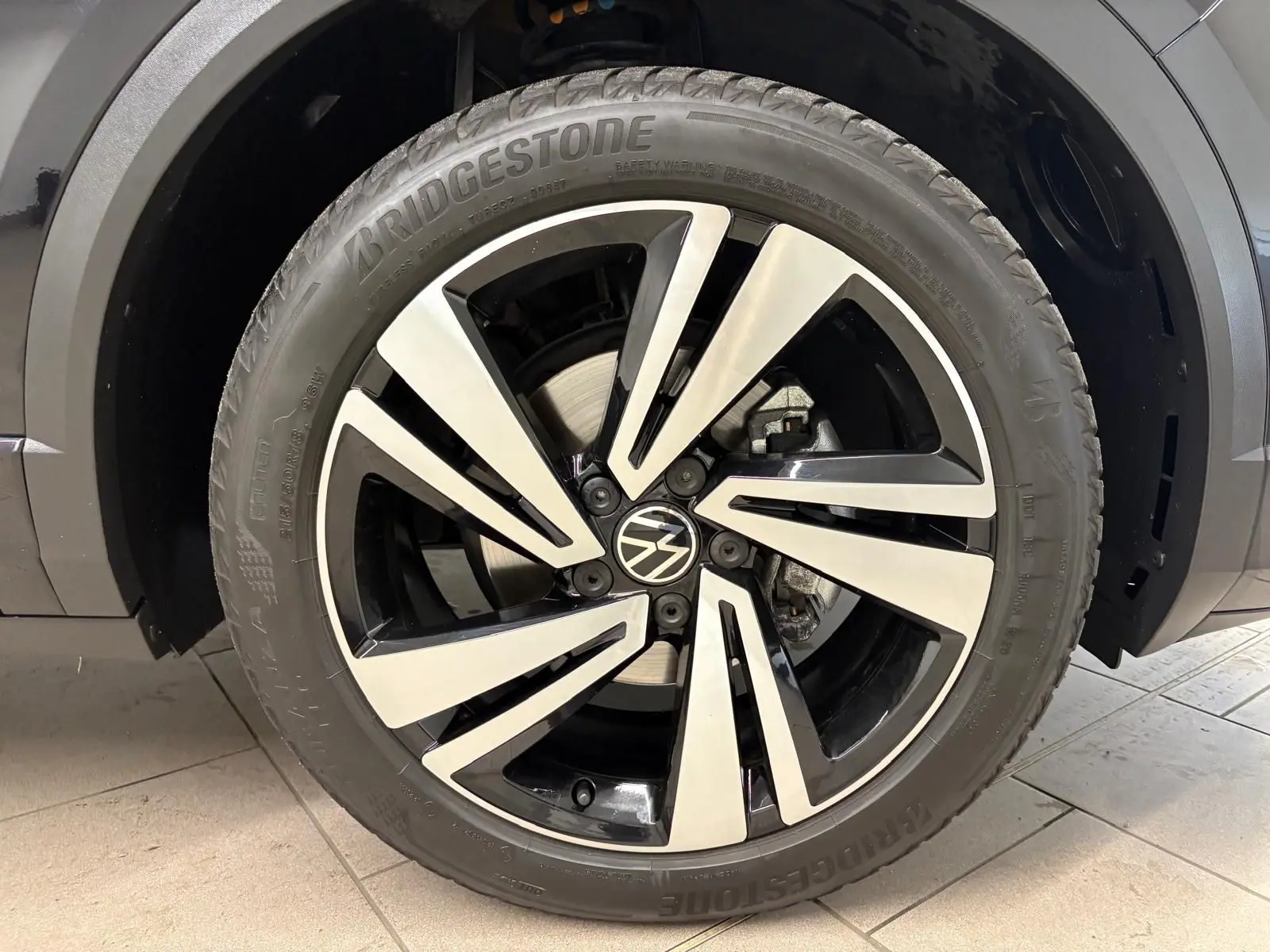 Gros plan sur la roue avant droite noire intense du Volkswagen T-Roc 1.5 TSI 150 DSG7 R-Line Edition avec jante alliage bicolore.