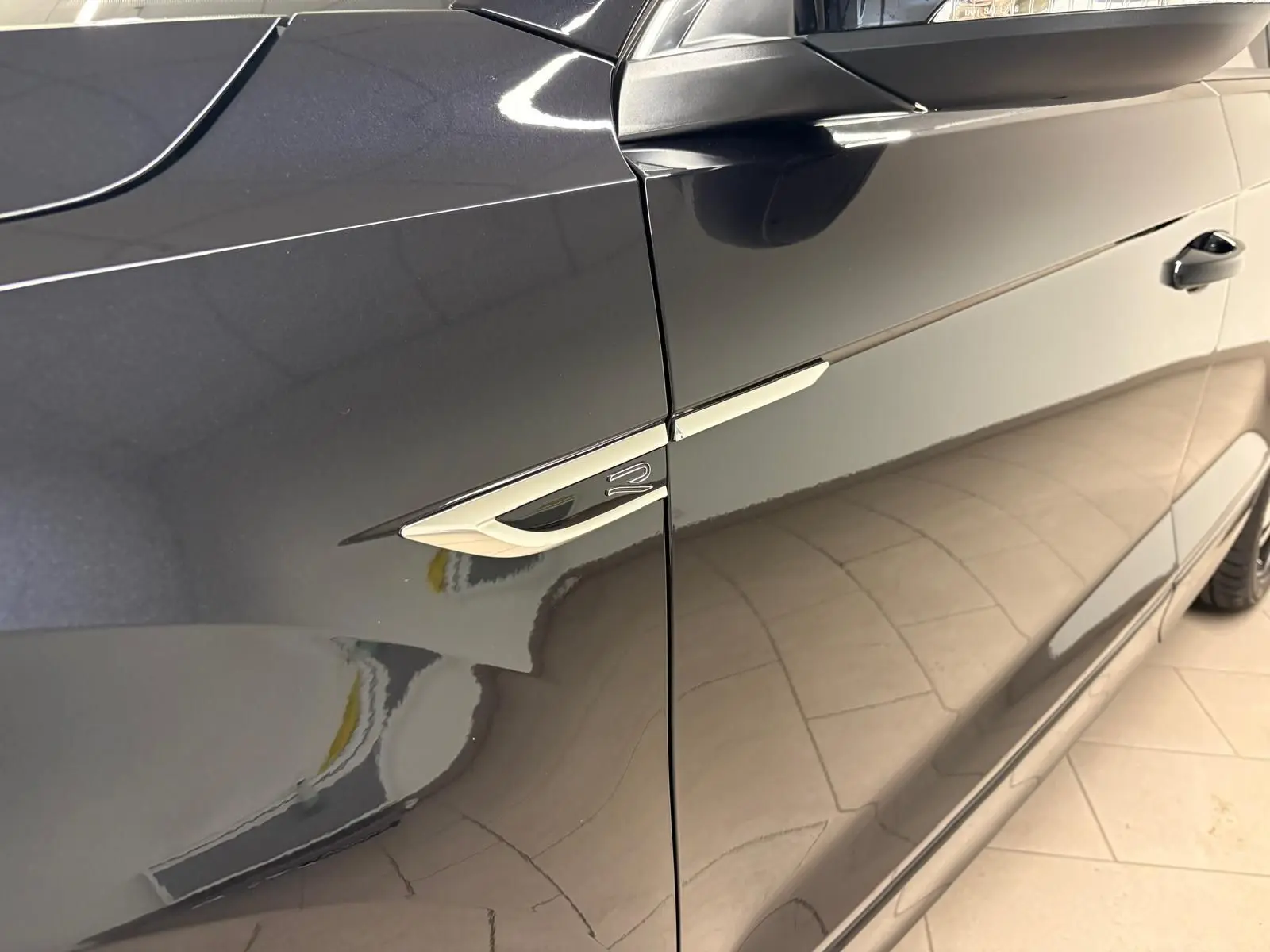 Vue latérale côté gauche du Volkswagen T-Roc noir intense, mettant en valeur l'emblème R-Line sur l'aile avant.