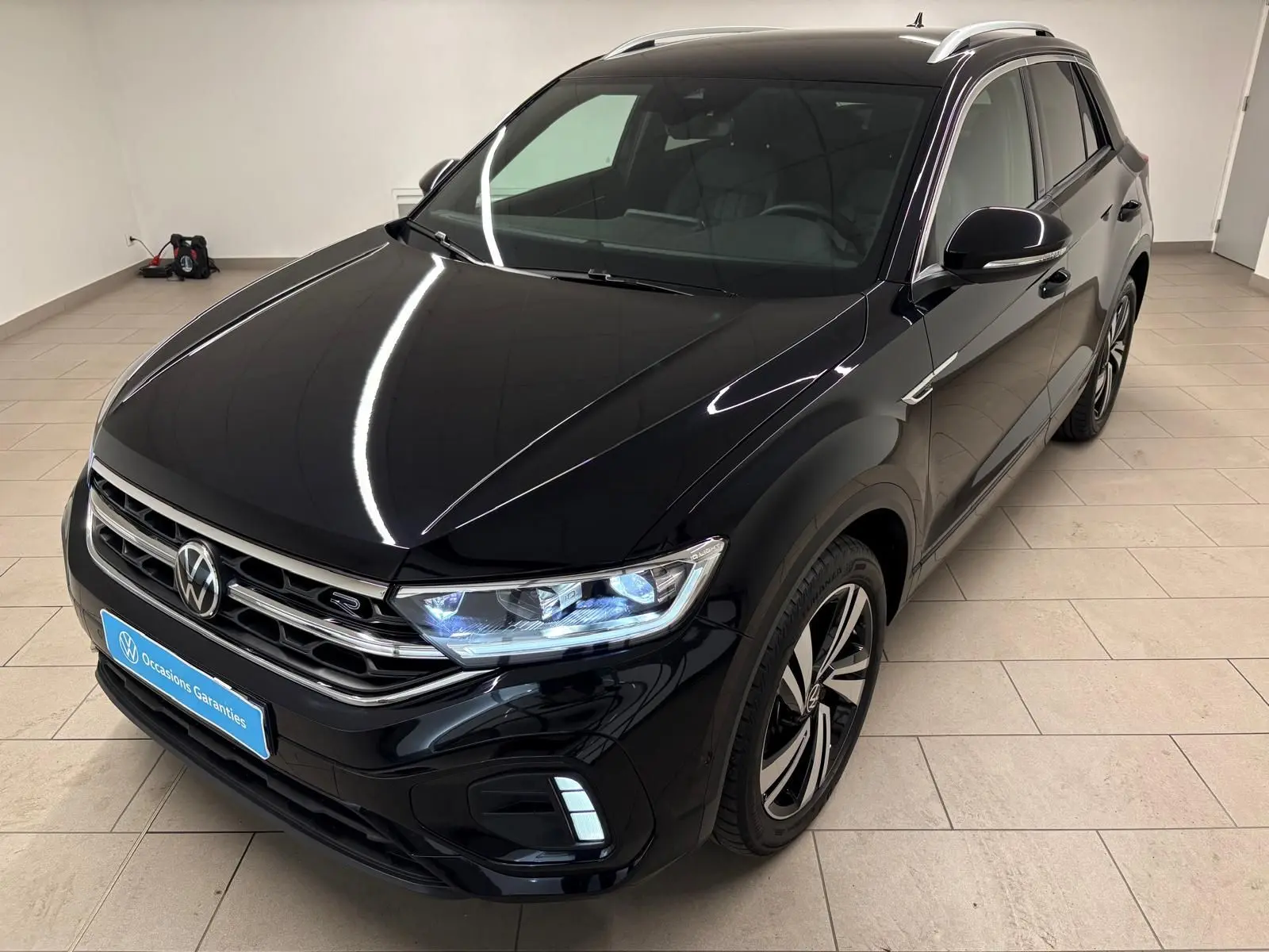 Volkswagen T-Roc noir intense en 3/4 avant droit, avec phares LED allumés et jantes R-Line distinctives.