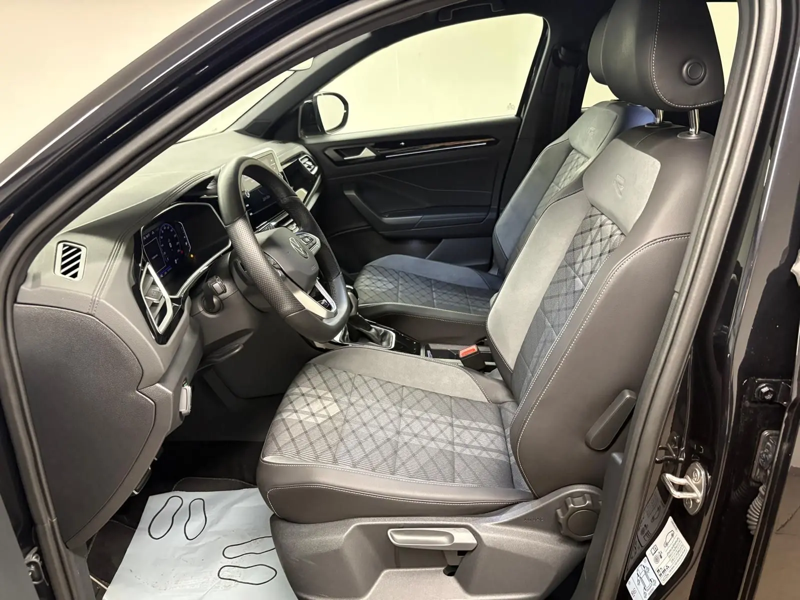 Vue intérieure côté conducteur du Volkswagen T-Roc 1.5 TSI R-Line noir intense, sièges avant en tissu et cuir avec surpiqûres.