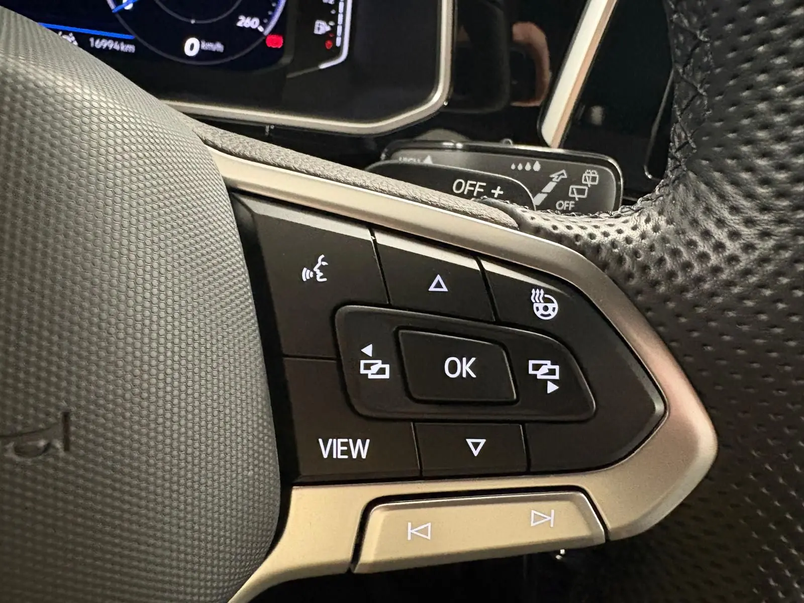 Gros plan sur les commandes du volant noir perforé du Volkswagen T-Roc 1.5 TSI 150 DSG7 R-Line Edition.