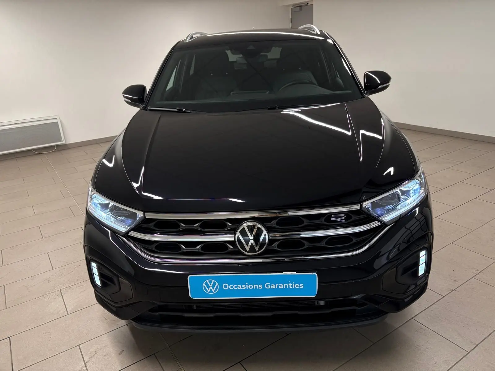 Volkswagen T-Roc noir intense vue de face, avec calandre chromée et phares LED allumés dans un intérieur neutre.