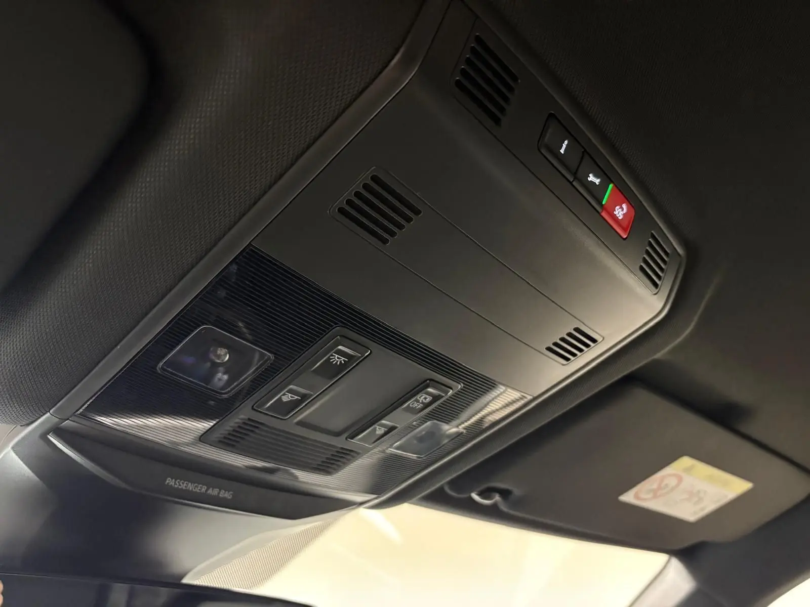 Vue en contre-plongée du plafonnier noir du Volkswagen T-Roc 2025 avec commandes d'éclairage et bouton SOS rouge.