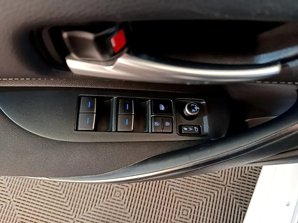 Gros plan sur la commande des vitres et rétroviseurs côté conducteur de la Toyota Corolla hybride blanche, intérieur noir.