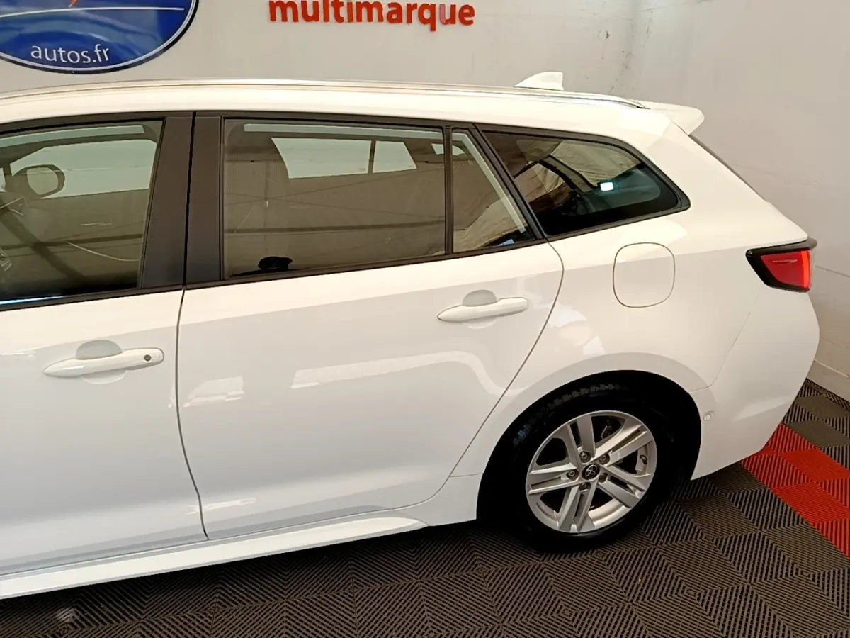 Vue latérale droite d'une Toyota Corolla hybride blanche, mettant en valeur les vitres teintées et les jantes alliage.